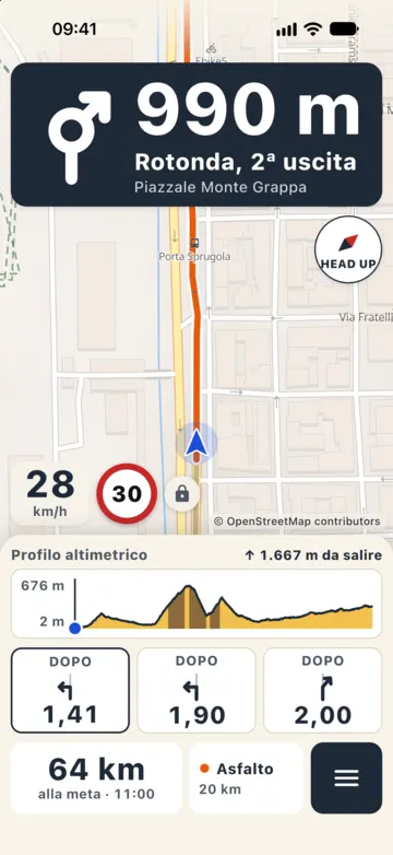 Guida di giorno in città: rotonda, seconda uscita tra 990 metri, 28 km/h con limite 30, tre riquadri con le svolte successive e 64 km alla meta con arrivo alle 11:00.
